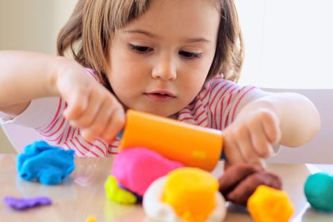 young girl plays with play dough using a roller