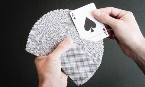 pair of hands holding a deck of cards, spread out. One hand holds an Ace.