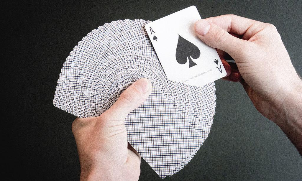 pair of hands holding a deck of cards, spread out. One hand holds an Ace.